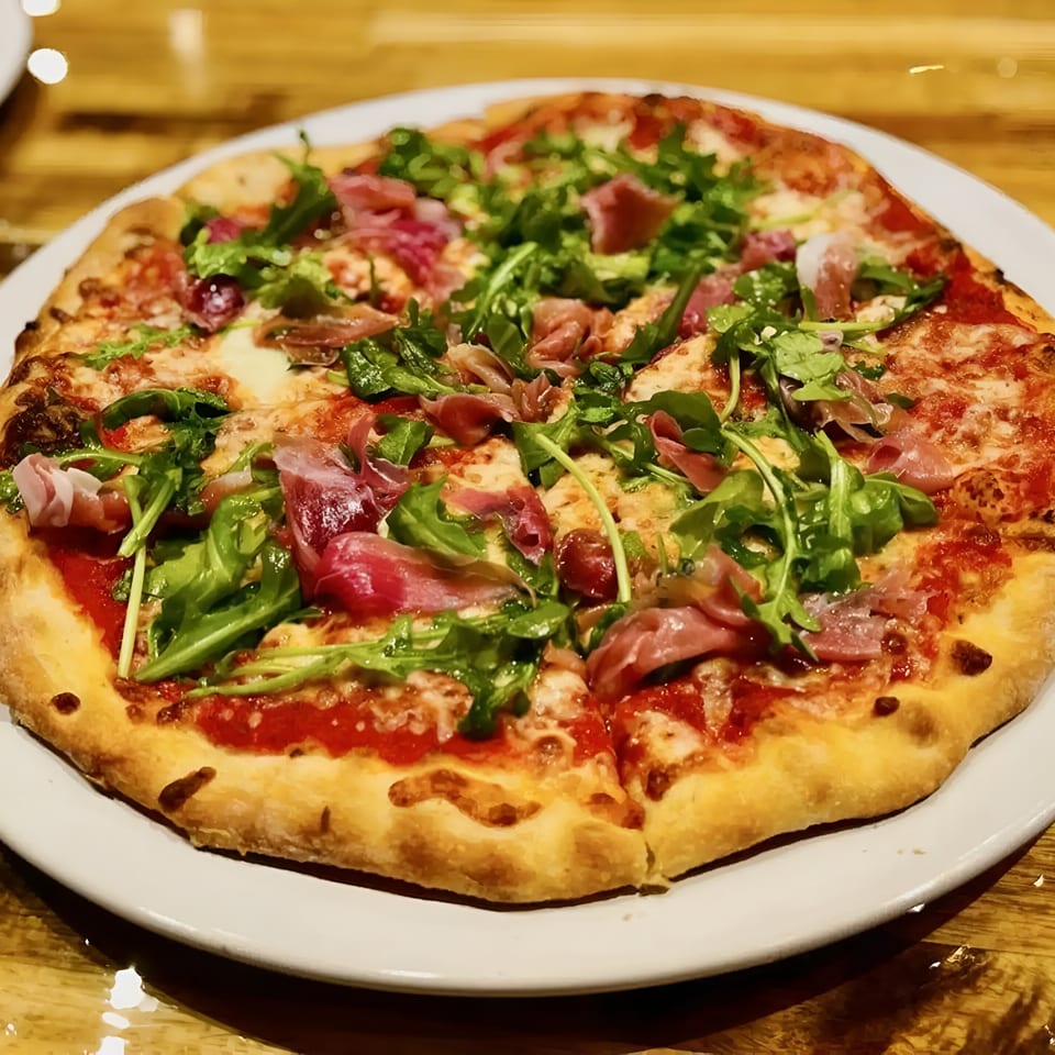 Cafe Napolina's Italian pizza topped with prosciutto, fresh arugula, and melted cheese on a white plate.