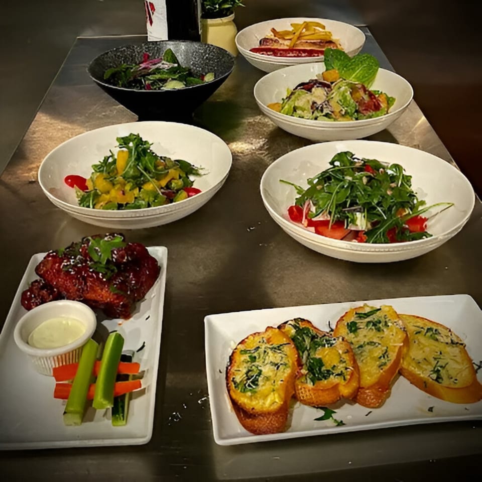 A table laden with various Italian dishes, including salads, garlic bread, and chicken wings.
