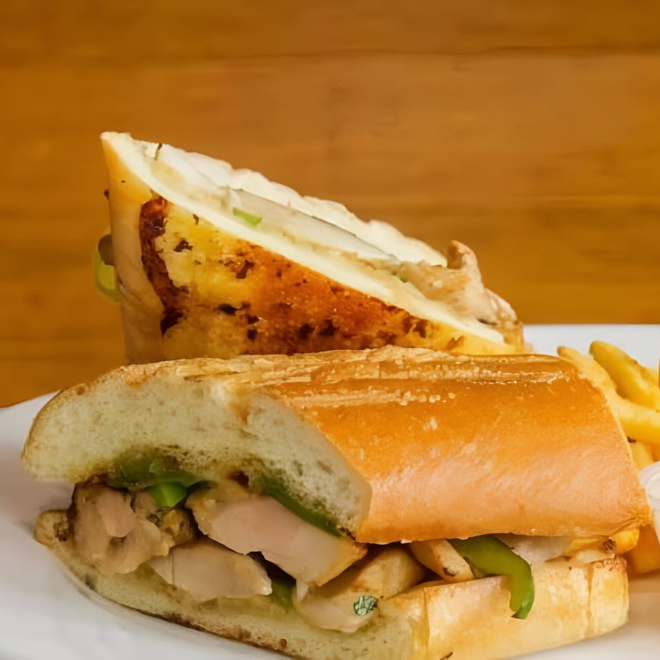 A chicken sandwich with green peppers and fries on a white plate at Cafe Napolina.