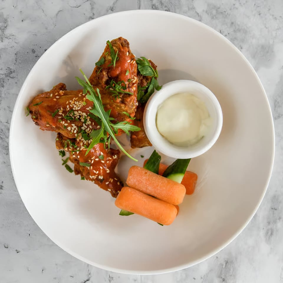 Cafe Napolina's chicken wings with sauce, sesame seeds, arugula, baby carrots, and dipping sauce.