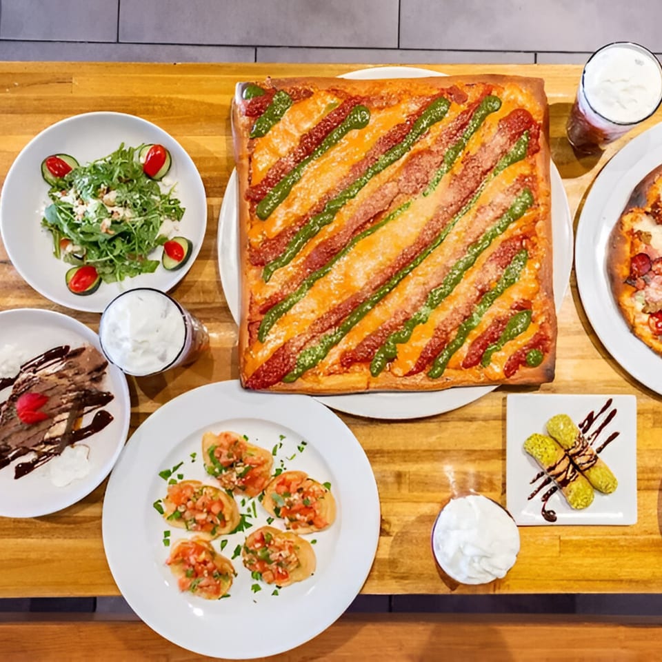 Overhead view of Cafe Napolina's Italian feast: square pizza, salad, bruschetta, dessert, and drinks.