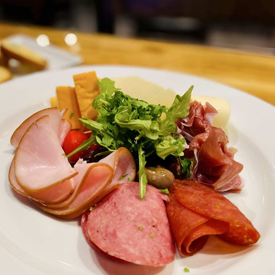 A Cafe Napolina charcuterie board with various meats, cheeses, olives, and arugula.